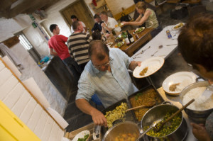 Volunteers dishing up dinner at Chyvarloe basecamp, The Stables, Penrose Estate, on a National Trust Working Holiday, Cornwall